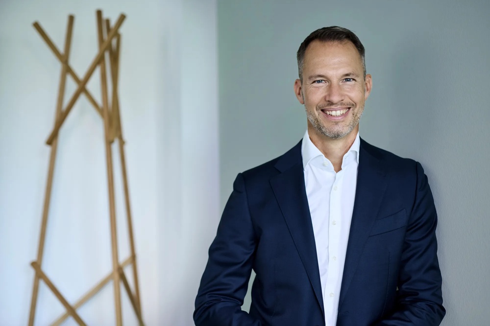 Michael Henn ist Global Head of Green Deal Infrastructure. Michael Henn lehnt gegen eine gruene Wand, neben ihm ist eine Metall-Skulptur.