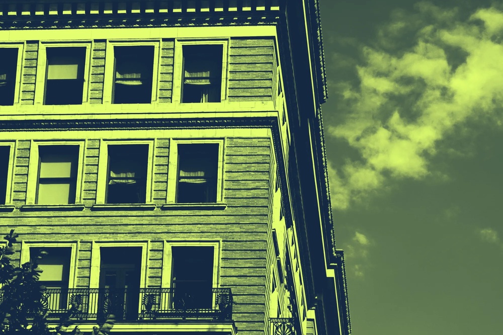 Fassade eines mehrstöckigen Gebäudes mit großen Fenstern und einem Balkon, vor einem bewölkten Himmel.