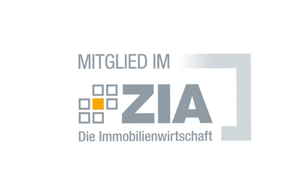 Logo aus zwei stilisierten Gebäudeformen – eine in Türkis-Blau, eine in Orange-Pink – mit dem weißen Schriftzug „Real Green Award" – Nachhaltigkeitsauszeichnung der Immobilienwirtschaft.