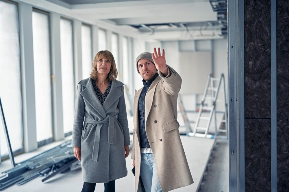 Eine Frau mit schulterlangem Haar trägt einen grauen Mantel und schaut nach oben.