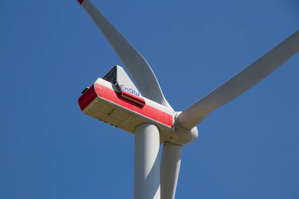 Eine weiße Windkraftanlage mit rotem Akzent vor klarem blauem Himmel.