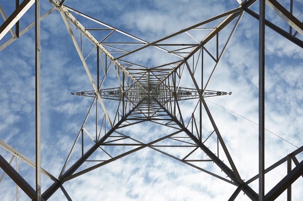 Blick von unten durch einen Strommast in den blauen Himmel mit weißen Wolken.