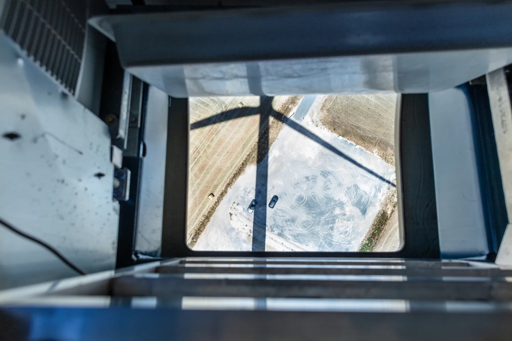 Eine Person steht auf einer Windkraftanlage und schaut auf ein Gerät, mit mehreren Windrädern im Hintergrund.