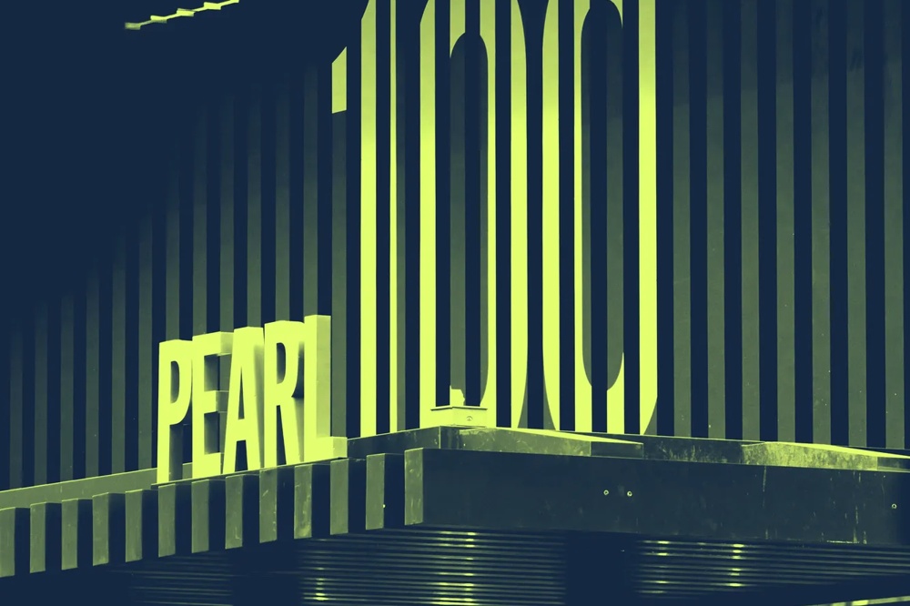 Schriftzug "PEARL 100" auf einem gestreiften Gebäude, darunter hängende Glühbirnen.