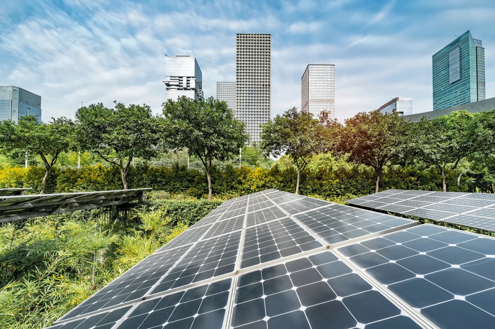 Solarmodule vor einer grünen Parklandschaft mit modernen Hochhäusern im Hintergrund unter blauem Himmel.