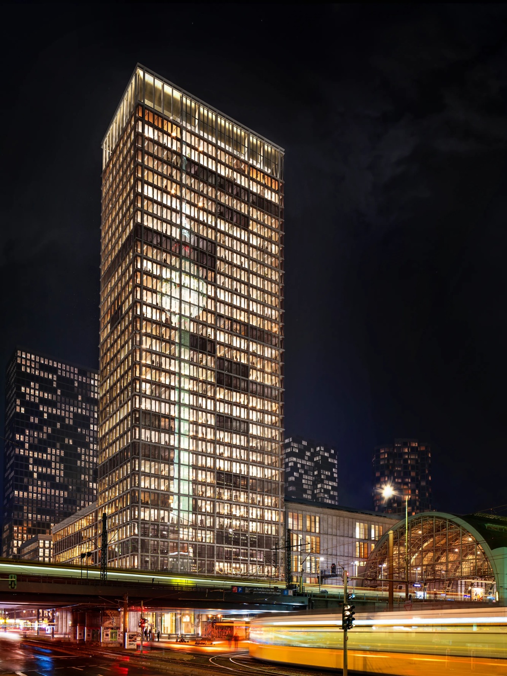 Illuminated city at night, yellow tram draws blurred lines in front of modern glass buildings and train station.