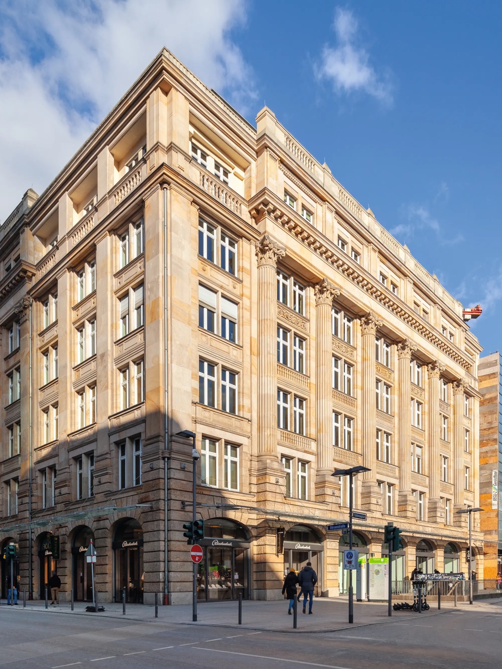 A large, historic building with many windows on a street corner under a blue sky.