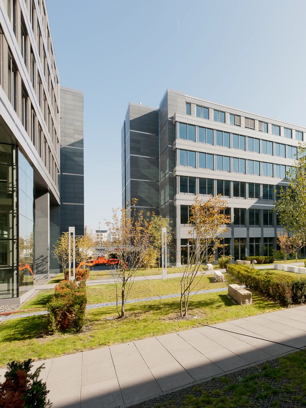 Moderner Bürokomplex mit Glasfassaden und gepflegtem Innenhof, umgeben von Bäumen und Hecken.