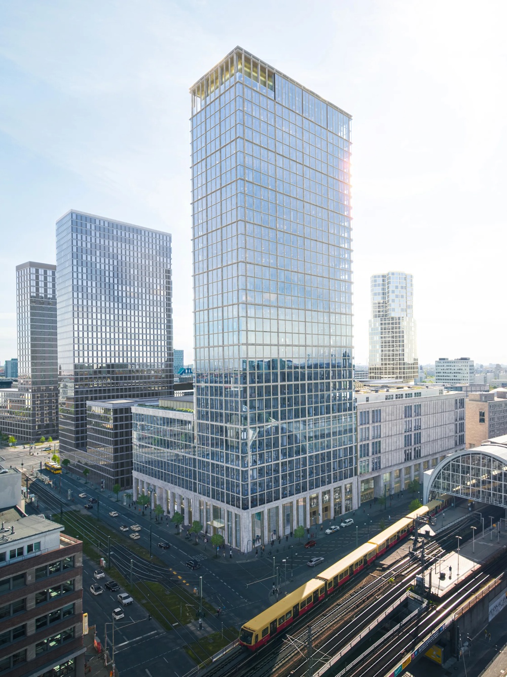 Modern city view with high-rise buildings, a large train station and a passing yellow subway under a clear sky.