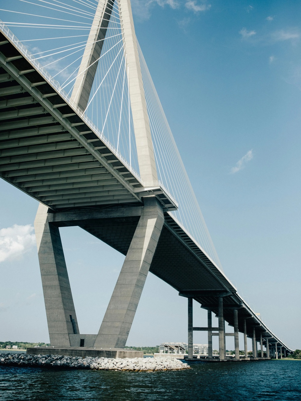 A large hanging bridge with inclined cables stretches over water under a blue sky.