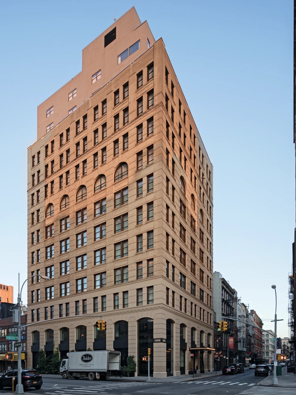 Ein großes, rotes Backsteingebäude an einer Straßenecke, umgeben von weiteren Gebäuden bei klarem Himmel.