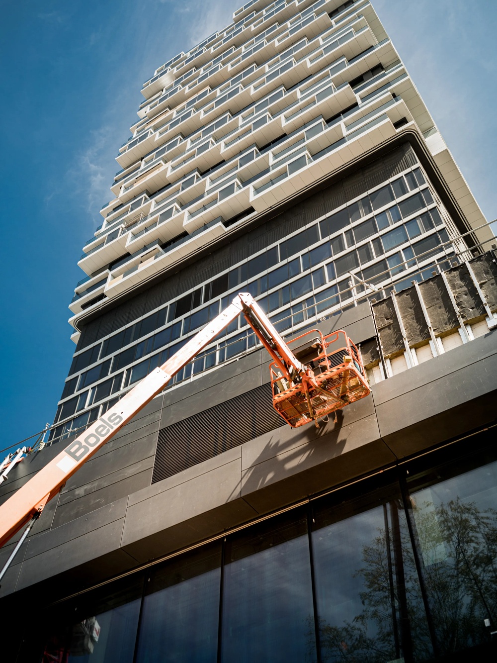 Ein modernes Hochhaus mit unvollendeter Fassade, ein orangefarbener Hebebühnenkorb hängt davor.
