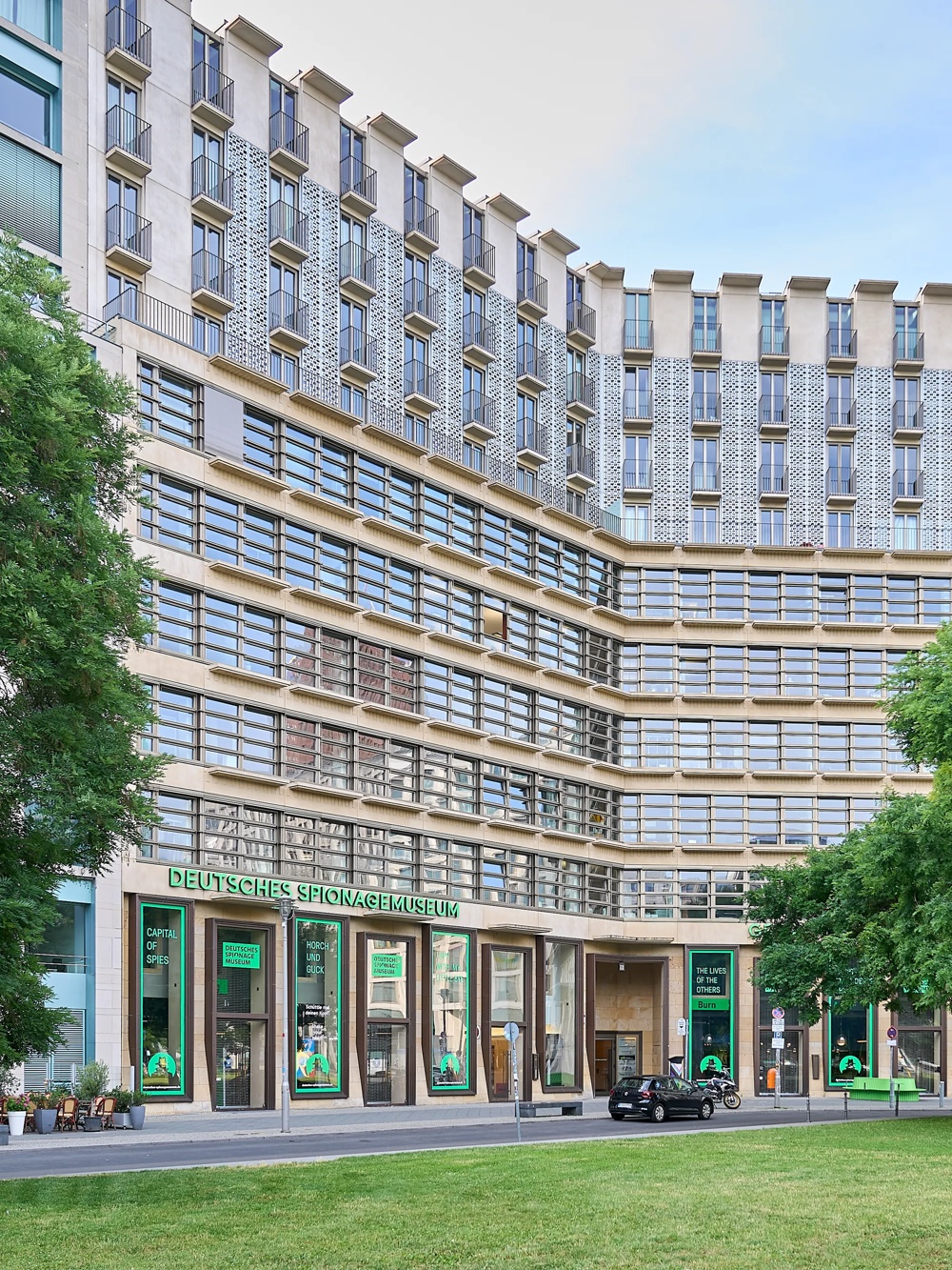 Ein modernes Gebäude mit vielen Fenstern, Bäumen und Rasenfläche davor, beschriftet als Deutsches Spionagemuseum.