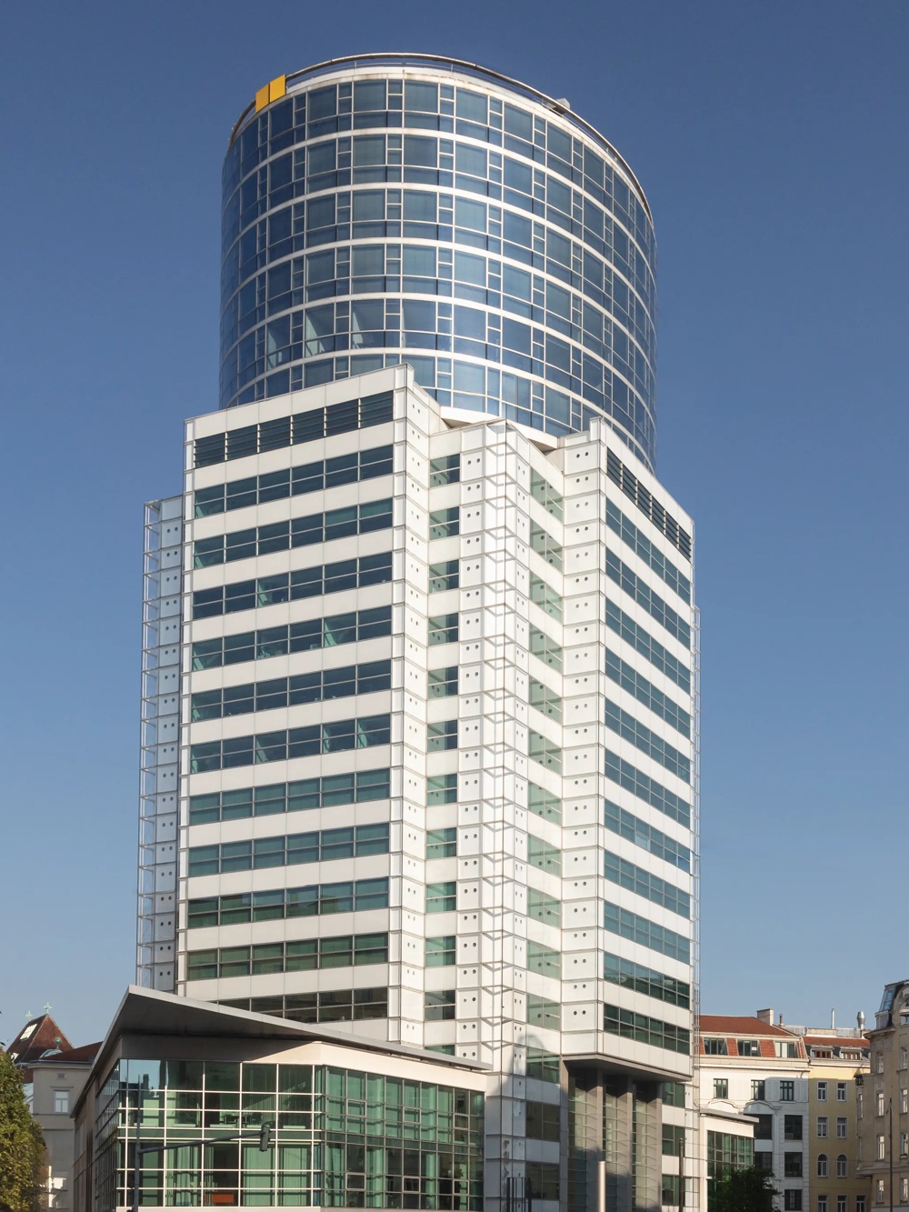 Ein modernes Hochhaus mit Glasfassade neben einem historischen Gebäude unter klarem, blauem Himmel.