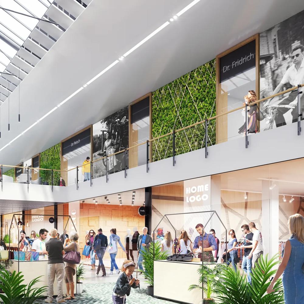 Helle Einkaufspassage mit Glasdach, Menschen flanieren, Pflanzen und Geschäfte auf beiden Seiten.