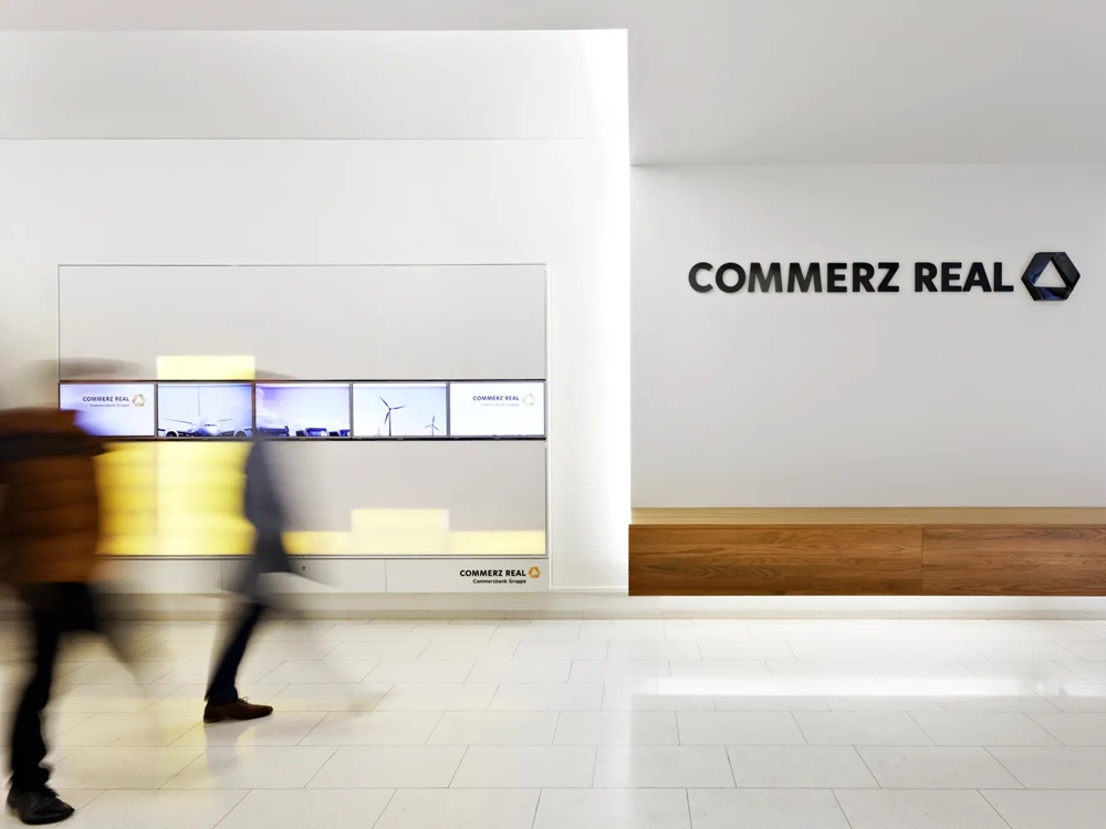 People passing by the wall in a modern office with the Commerz Real logo.