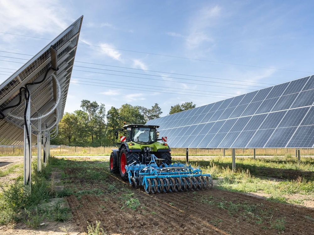 Landwirtschaftliche Maschine arbeitet zwischen Reihen von Solarmodulen.