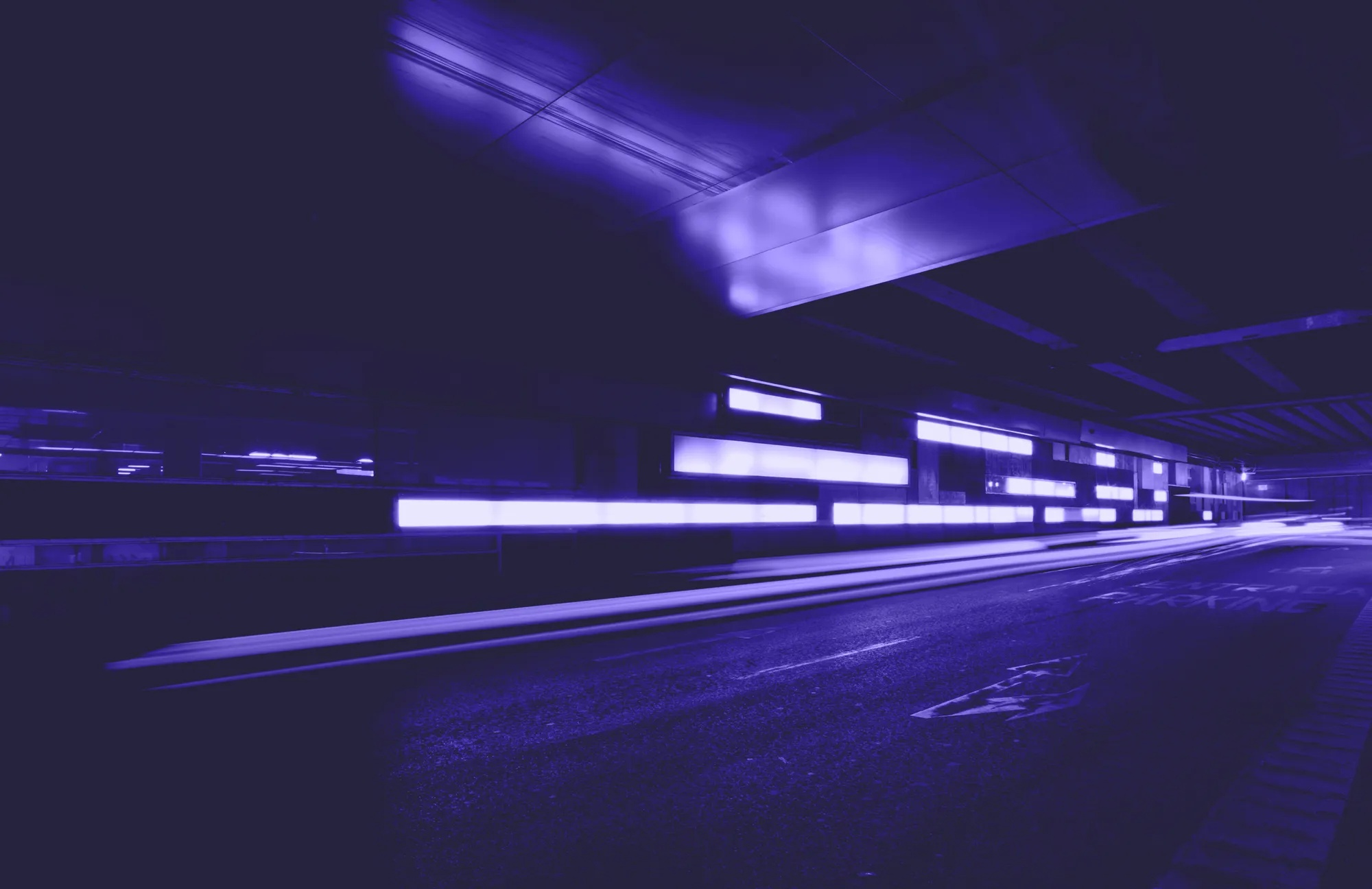 Dunkle Straße mit violetten Lichtern an den Wänden und verschwommenen Lichtstreifen von vorbeifahrenden Autos.