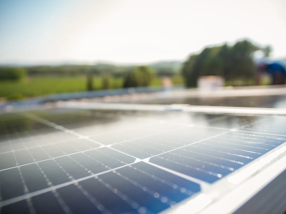 Solarpanel auf einem Dach mit unscharfem, grünen Landschaftshintergrund bei sonnigem Wetter.