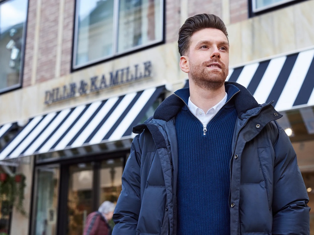 Ein Mann in blauer Jacke steht vor einem Geschäft mit schwarz-weiß gestreifter Markise.