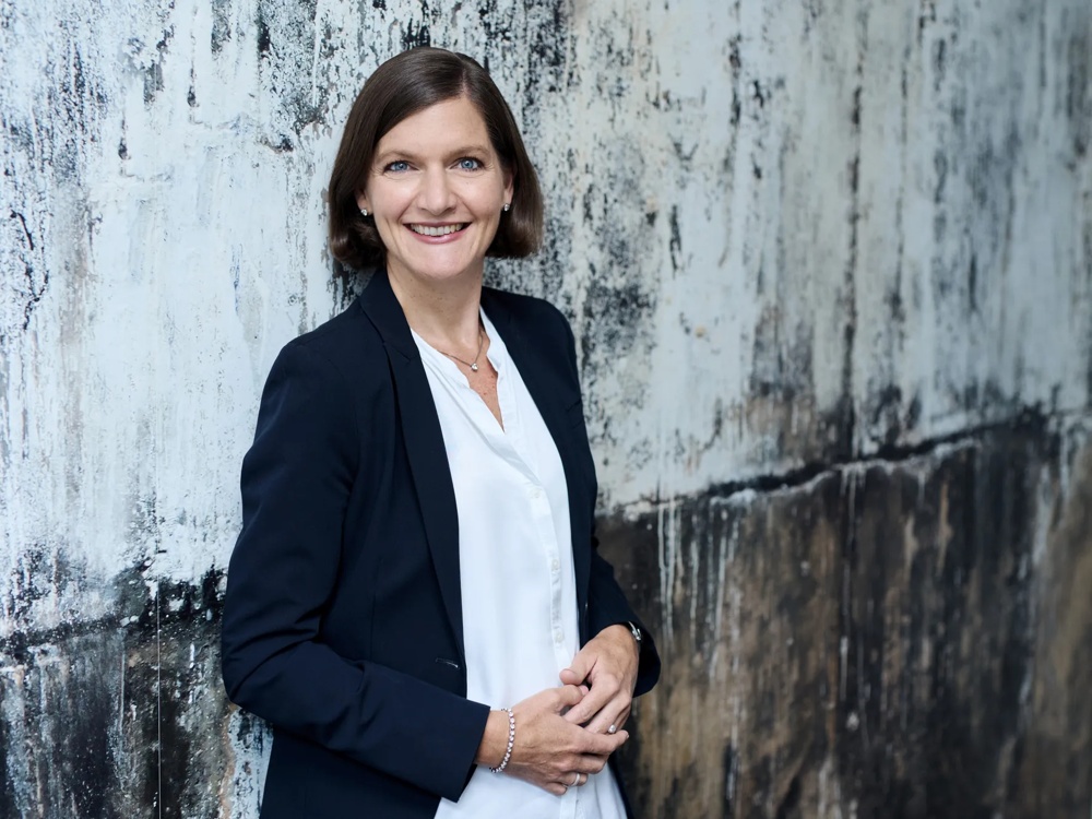 Nadia Eichelberger ist Global Head of Real Estate Office and Industrial. Nadia Eichelberger lehnt gegen eine graumelierte Wand.