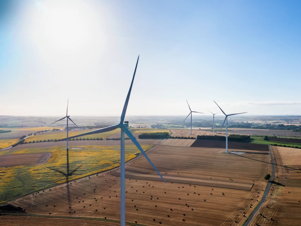Windräder auf einem Feld bei Sonnenuntergang, mit weitläufigem Himmel und sanften Wolken.