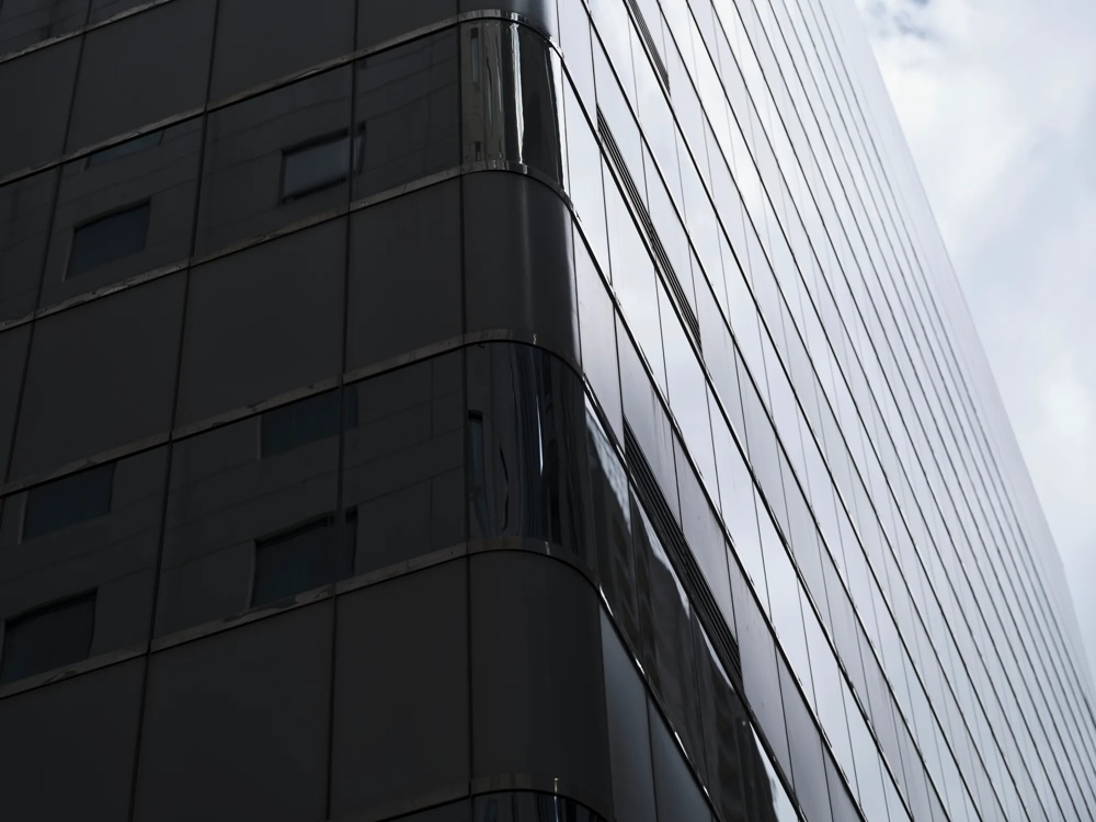 Ein modernes Hochhaus mit verspiegelter Glasfassade unter bewölktem Himmel.