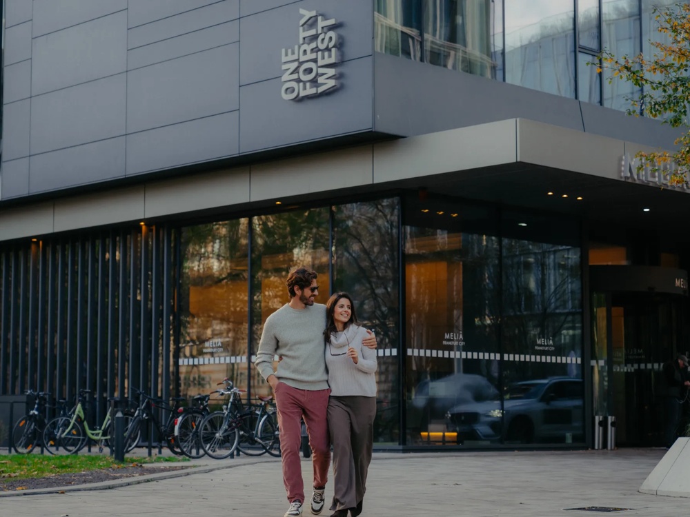 Zwei Personen gehen im Außenbereich vor einem Gebäude.