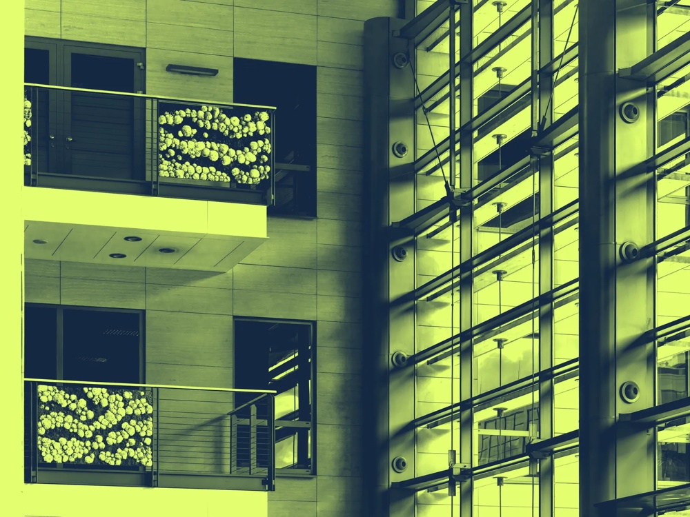 Balkon mit Blumendekoration an modernem Gebäude, neben Glasfassade mit Schattenlinien.