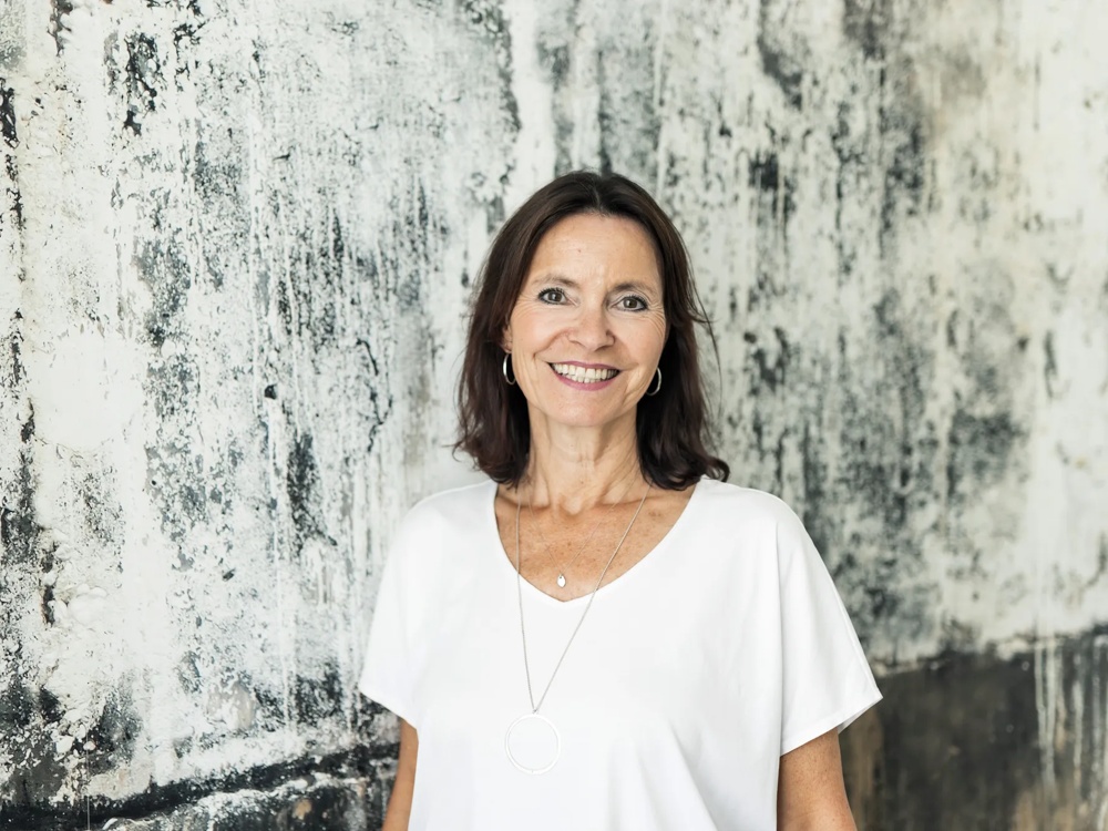 A smiling woman in front of a black and white textured wall.