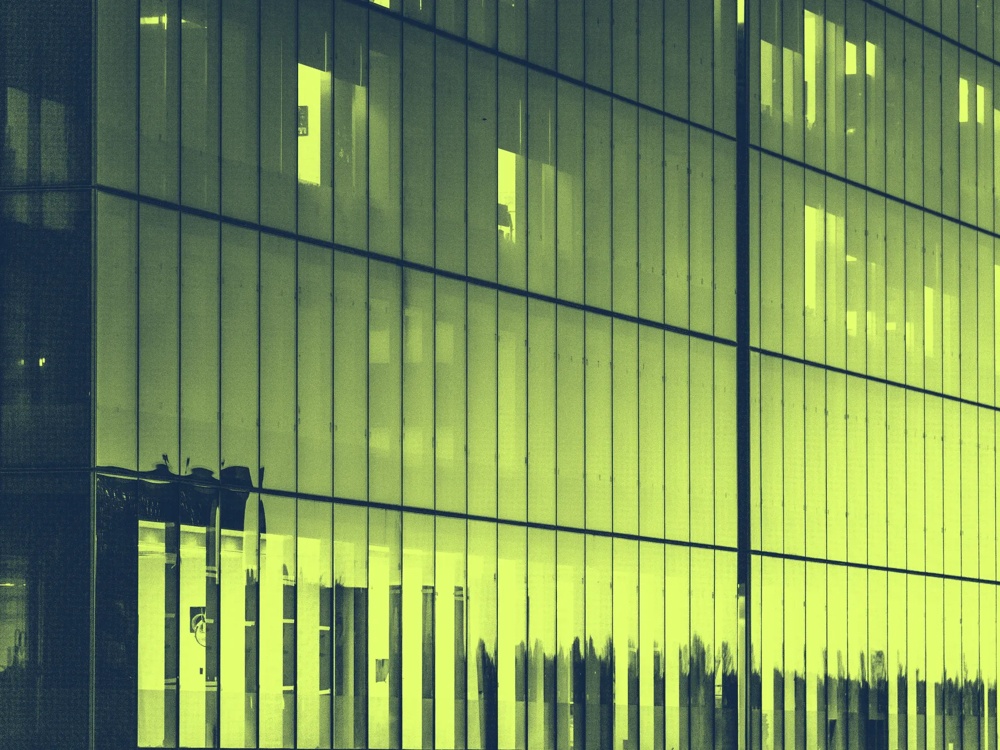 Glasfassade eines Gebäudes mit reflektierenden vertikalen Linien in grünlichem Licht.