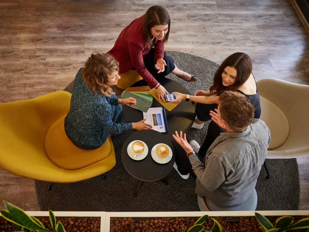 Four people are sitting around a table with coffee and documents while discussing.