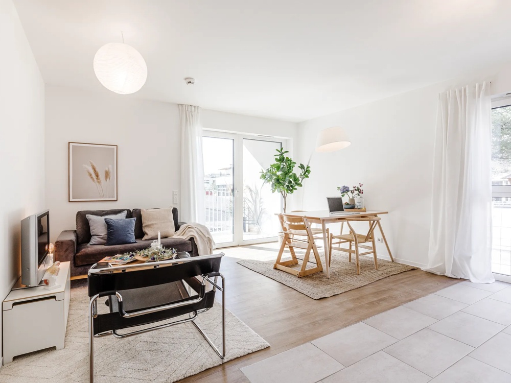 Helles Wohnzimmer mit Sofa, Tisch, Stuhl, großen Fenstern und Pflanzen. Moderne, minimalistische Einrichtung.