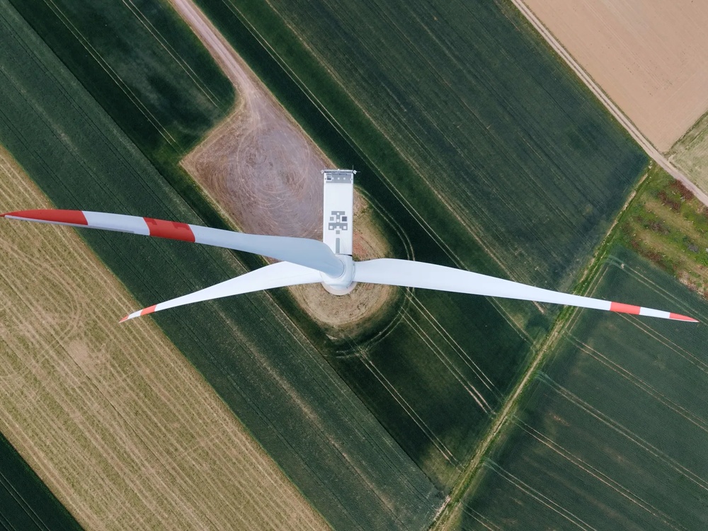 Zwei Windräder stehen auf einem weiten Feld unter bewölktem Himmel bei Sonnenuntergang.