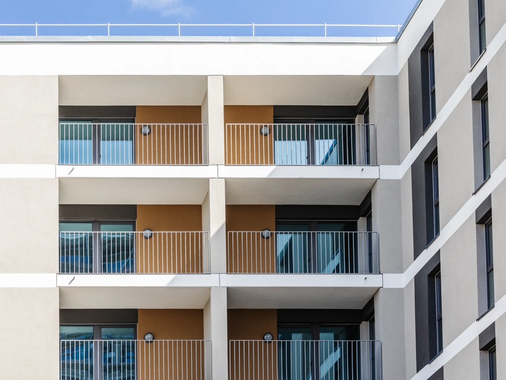 Moderne Wohnhausfassade mit übereinanderliegenden Balkonen mit Metallgeländern und großen Fenstern.