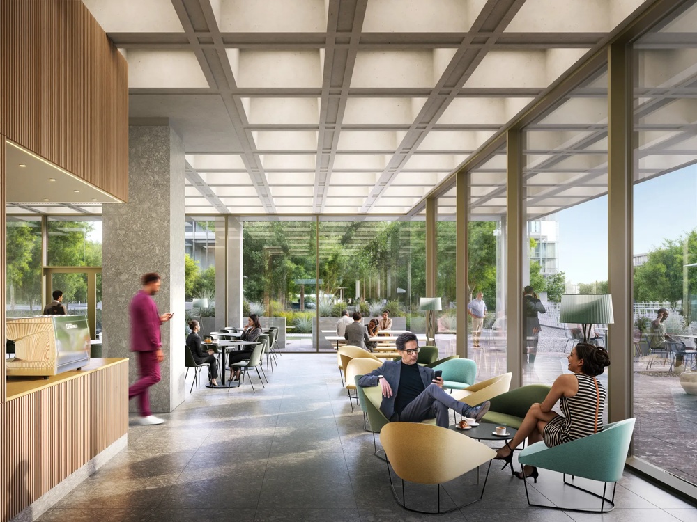 Modern lounge with large windows, people sitting on colourful armchairs, green trees visible outside.