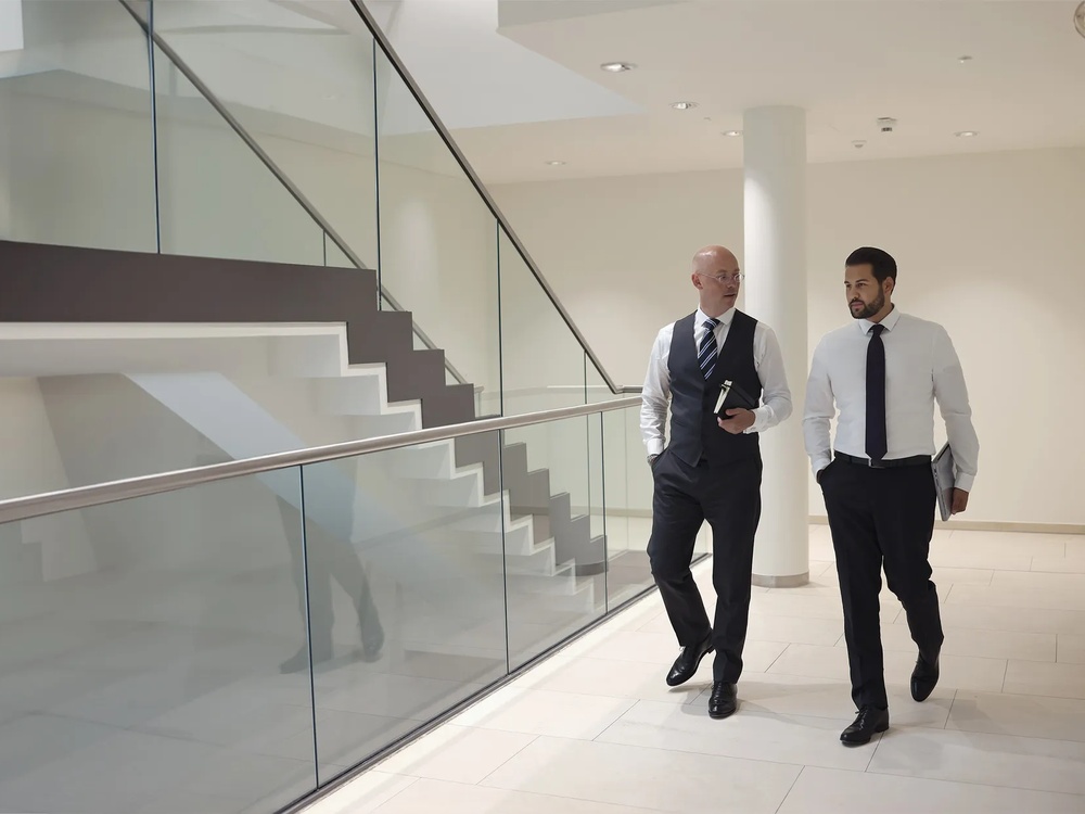 Zwei Büromenschen unterhalten sich beim Laufen angeregt im Treppenhaus eines Bürogebäudes.