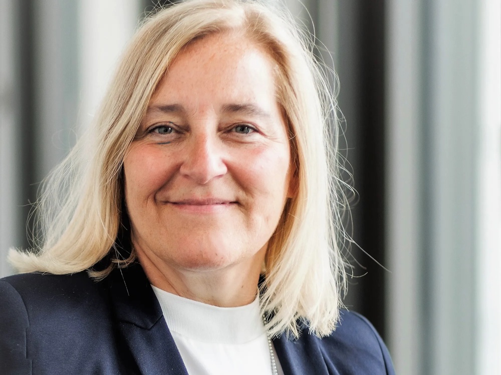 A smiling woman with blonde hair wearing a dark jacket and a white top.