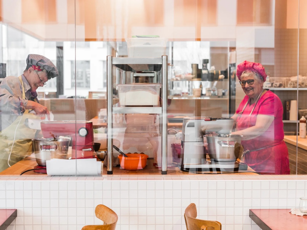 Zwei Personen backen in einer modernen Küche, umgeben von Rührgeräten und Regalen.