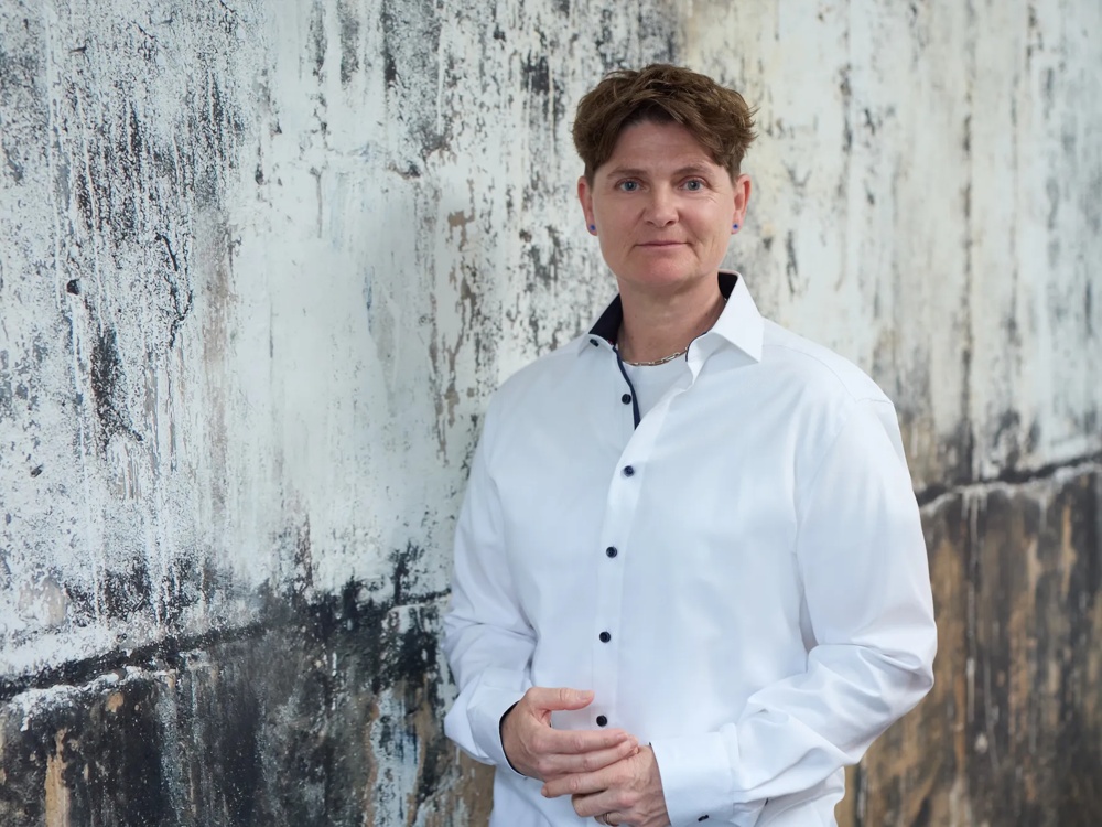 Person in white shirt standing in front of a weathered, textured wall.