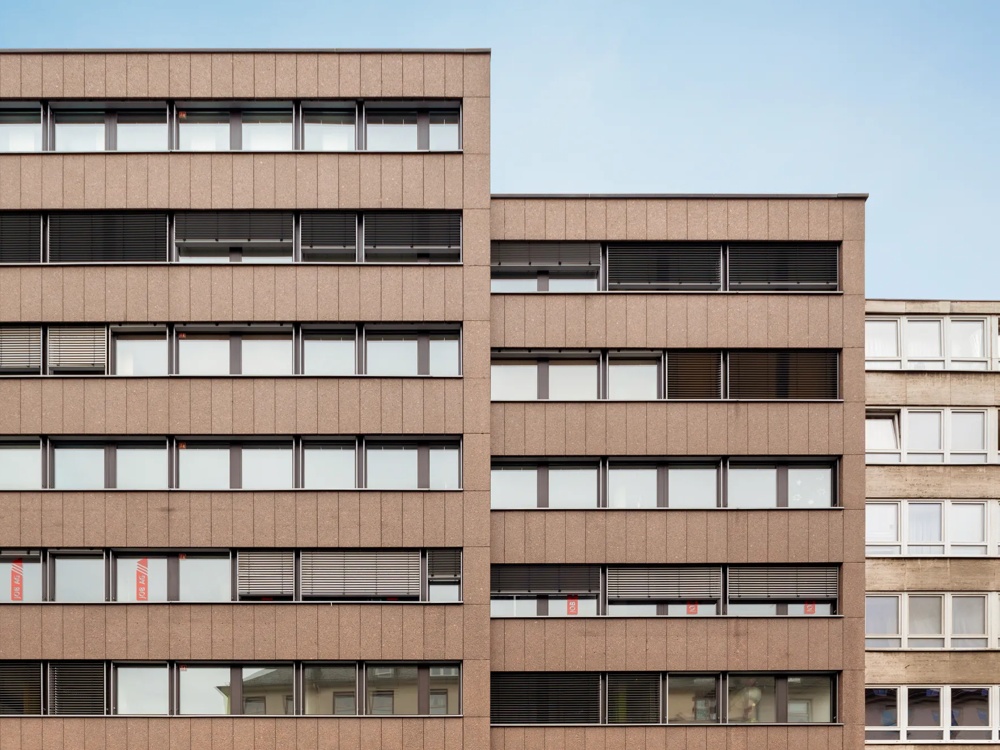 Brown, modern building with several floors and windows, blue sky in the background.