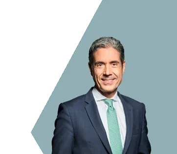 Ein Mann im Anzug mit türkisfarbener Krawatte lächelt vor einem blauen Hintergrund.