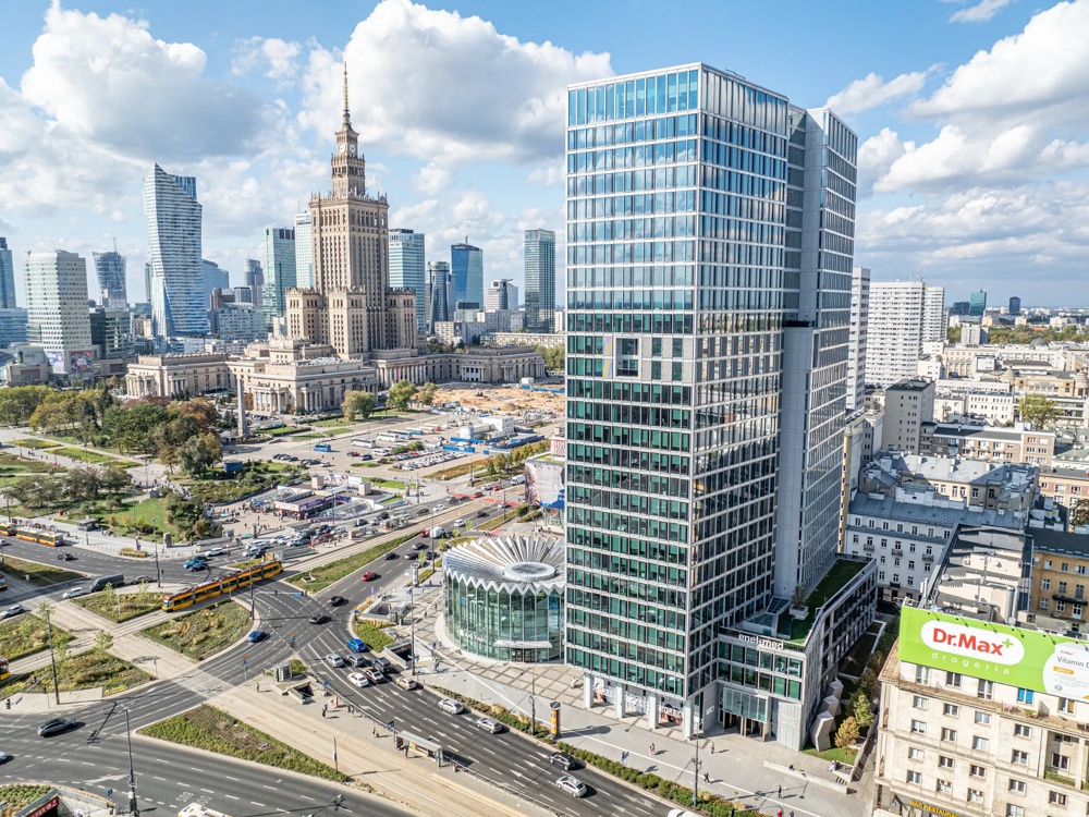 Stadtsilhouette mit Hochhäusern, einem historischen Gebäude und belebten Straßen unter blauem Himmel.