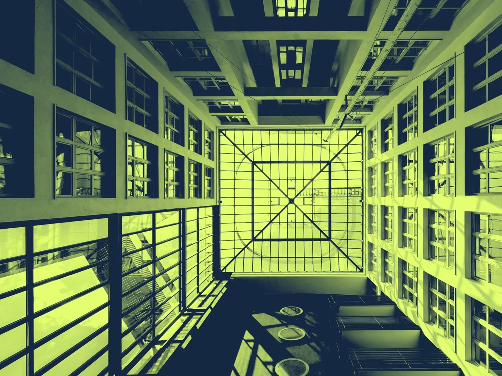 Blick nach oben in einen modernen Innenhof mit Glasdach und symmetrischen Fenstern, in Grün- und Gelbtönen gefärbt.