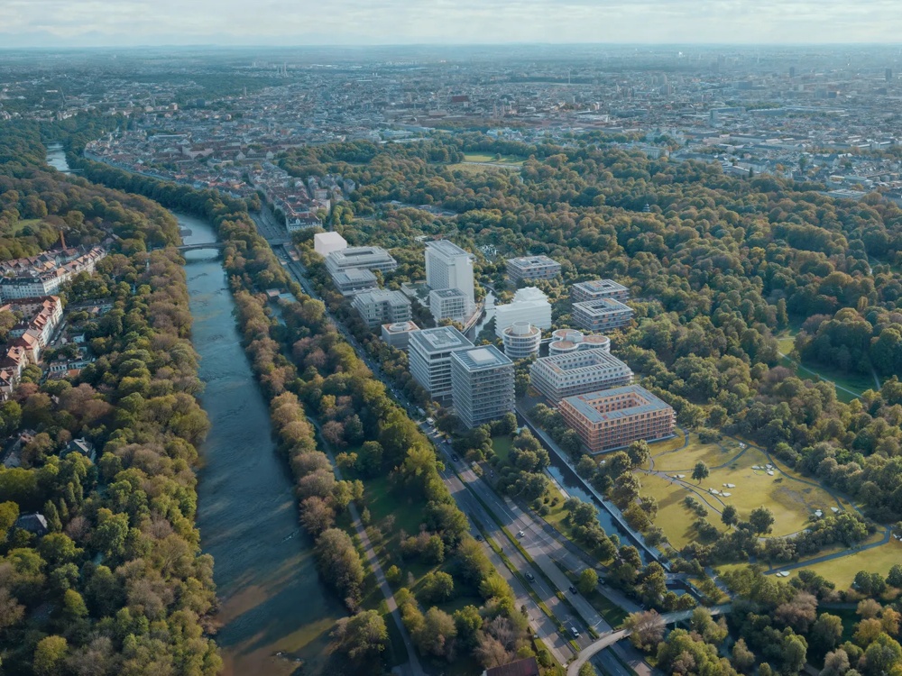 Luftaufnahme einer Stadt mit Fluss, umgeben von Bäumen und modernen Gebäuden, bei klarem Himmel.