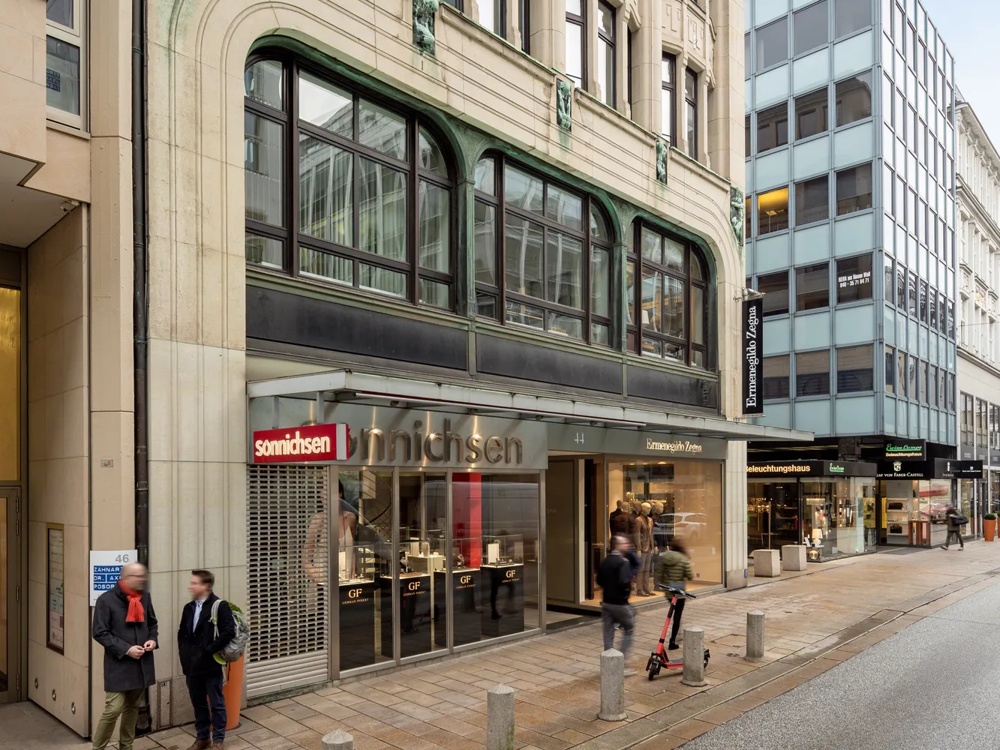 Mehrstöckiges Gebäude mit historischer Fassade, großen Fenstern und Geschäften im Erdgeschoss in einer belebten Straße.