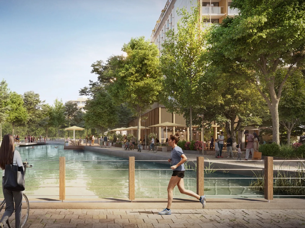 A woman riding a bike and jogging by a pond in a park with trees and a café.