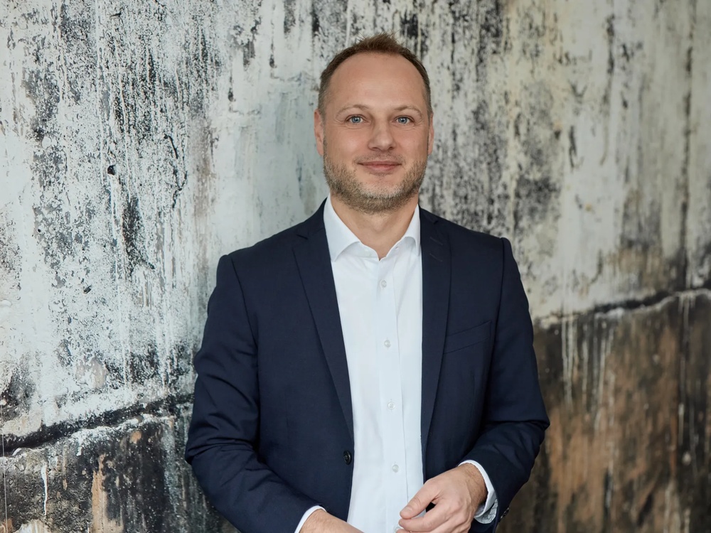 A man in a suit stands casually in front of a marbled wall.