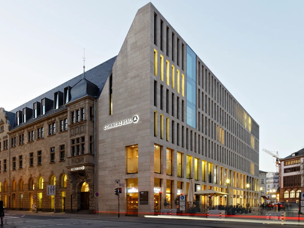 Modernes Gebäude mit Glasfassade und historischem Teil daneben, beleuchtet in der Dämmerung.