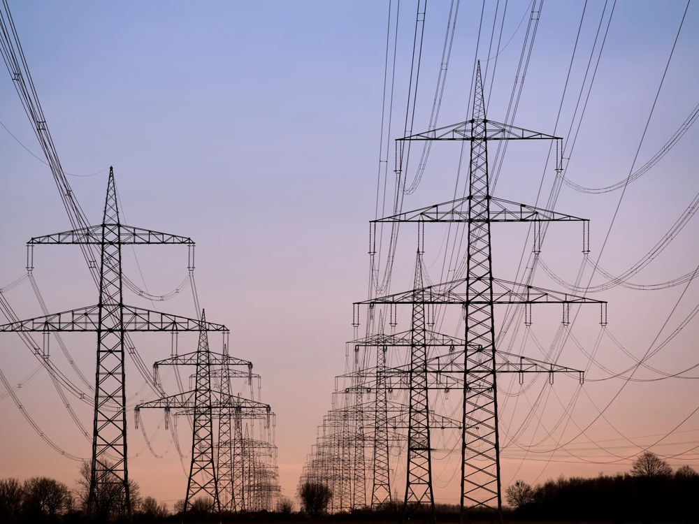 Hochspannungsmasten vor einem violetten Himmel bei Sonnenuntergang, umgeben von Bäumen.